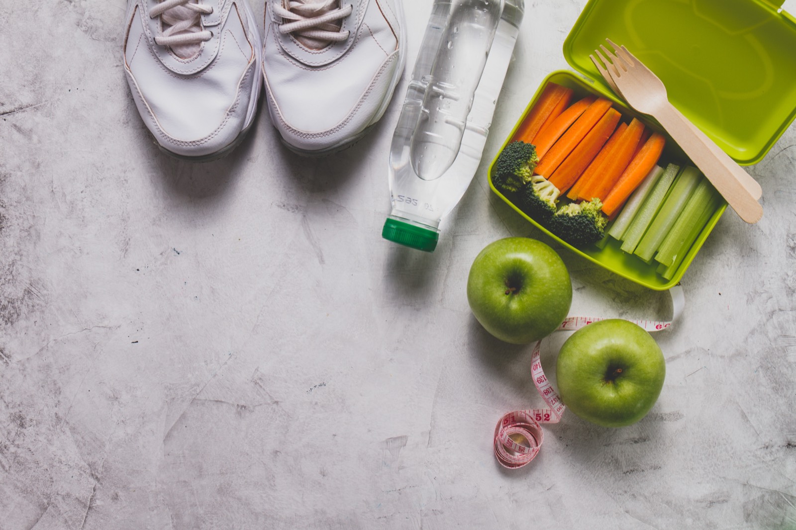 Tenis, botella de agua, manzanas, cinta métrica y verduras en una lonchera